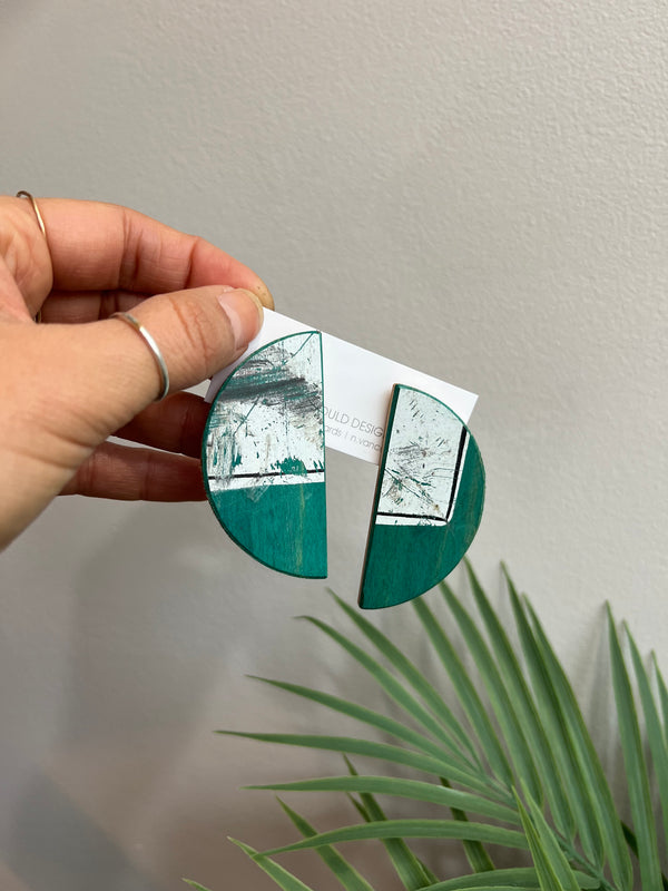Hand holding a circular mirror with green and silver design against a neutral background