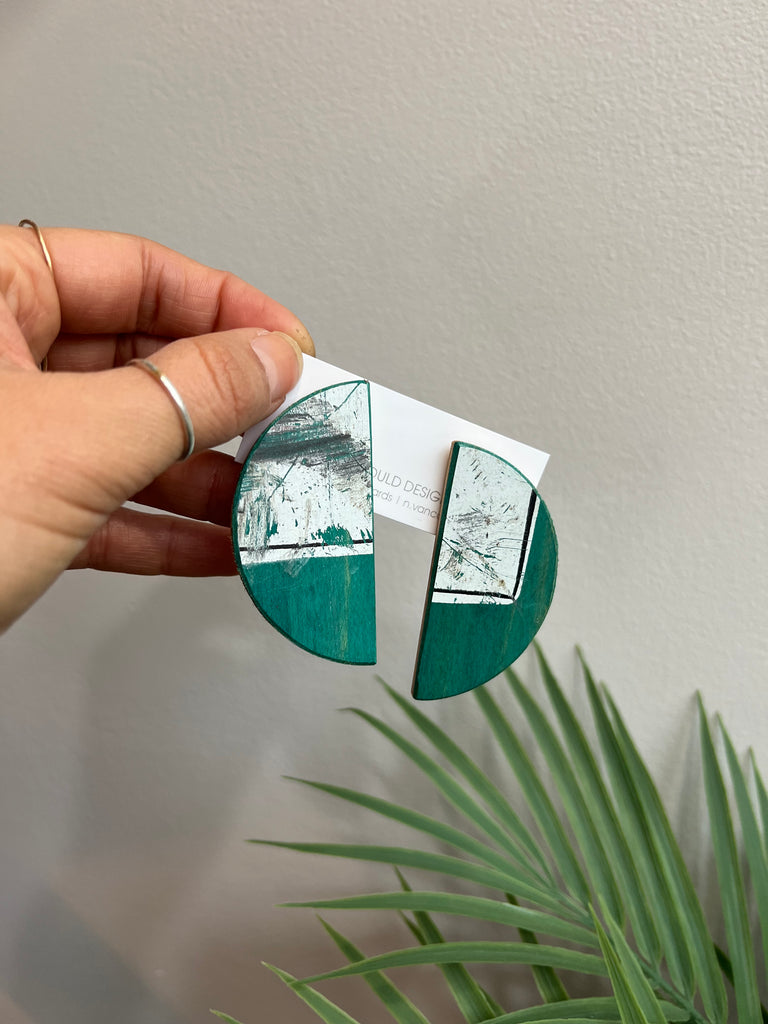 Hand holding a circular mirror with green and silver design against a neutral background