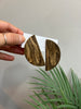 Wooden earrings held by a hand with a plant in the background