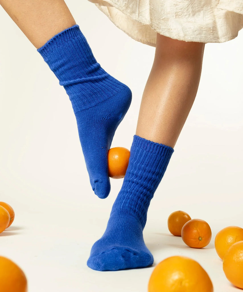 Blue socks worn by a person with oranges on a light background